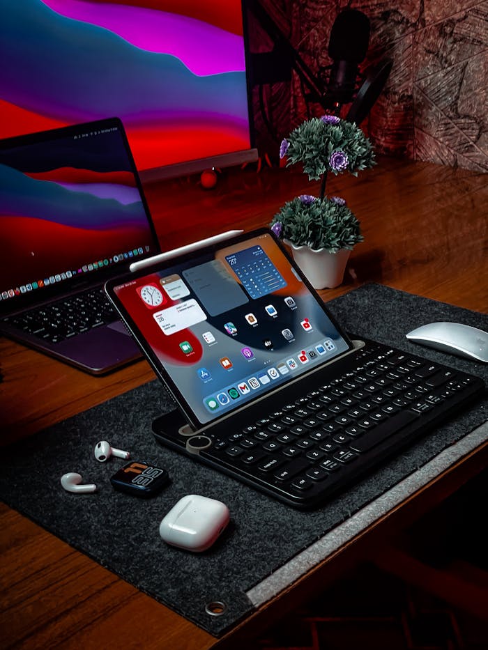 A sleek and modern workspace featuring an iPad with keyboard, MacBook, wireless mouse, and tech accessories on a wooden desk.